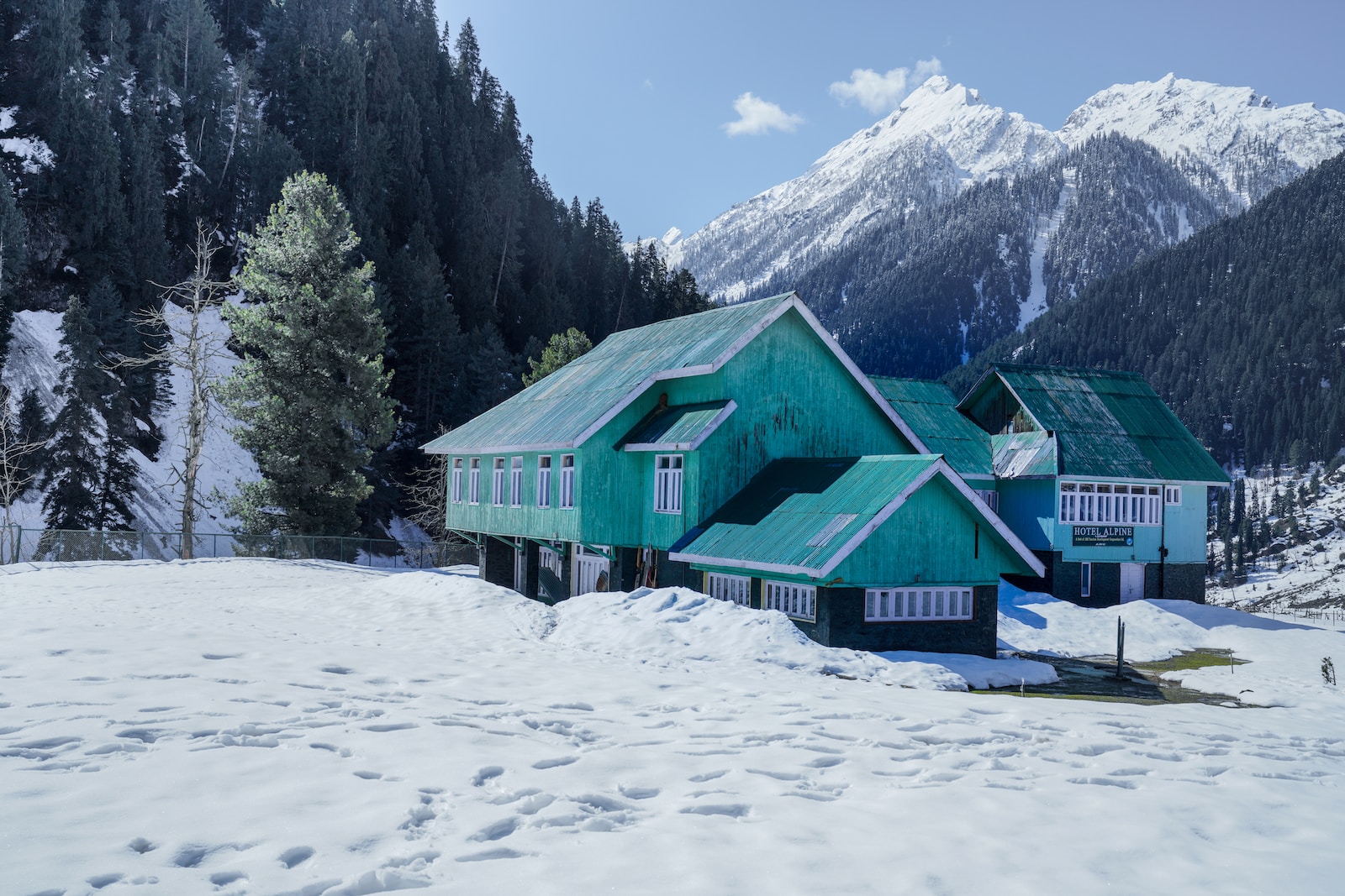 green wooden house on snow covered ground near green trees and mountain during daytime